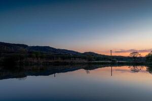 Sunset over a lake with young green grass on the banks and reflecting trees in the water photo