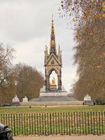 A statue of a man sitting on a bench in front of a park photo