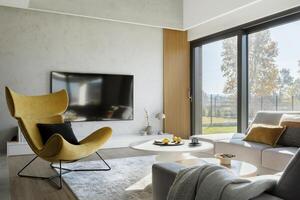 Modern living room interior design with corner beige sofa, creative rounded coffee tables, mustard armchair and personal accessories. Panoramic windows. Template. photo