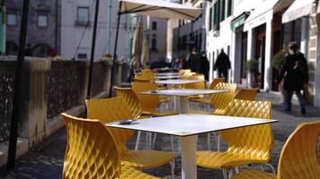 White open cafe tables stand among yellow chairs on sidewalk video