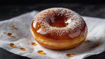 A glazed donut topped with coconut flakes, resting on parchment paper with syrup drizzles. photo