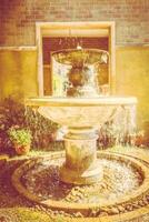 A fountain in a courtyard with a stone wall photo