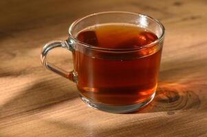 Warm cup of freshly brewed herbal tea resting on a rustic wooden table in soft afternoon light photo
