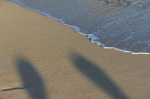 Two figures create shadows while frolicking by the shore as gentle waves lap against the sandy beach photo