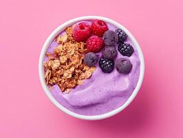 A bowl of blueberry yogurt with granola and berries on a pink background photo