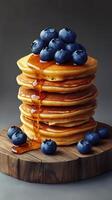 Stack of fluffy pancakes topped with blueberries and syrup on a wooden surface photo
