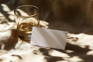 A clear glass with amber liquid next to a blank card on a softly lit table in a cozy setting photo