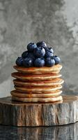 Stack of fluffy pancakes topped with blueberries and syrup on a wooden surface photo