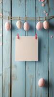 Colorful Easter eggs hanging on a string against a rustic blue wooden background with a blank card photo