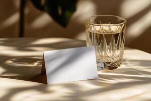A clear glass with amber liquid next to a blank card on a softly lit table in a cozy setting photo