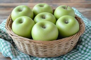 Fresh green apples in a woven basket on a checkered cloth resting on a wooden table photo