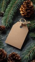 Blank kraft label surrounded by pine branches and cones on a dark stone surface photo