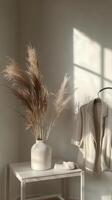 Cozy white knit sweater displayed on a hanger beside a stylish vase with dried pampas grass photo