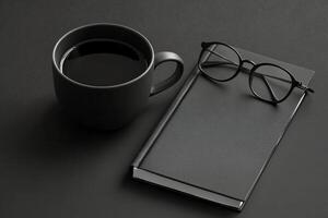 A dark workspace with a black coffee mug and glasses beside an open notebook during evening hours photo