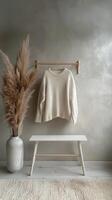 Cozy white knit sweater displayed on a hanger beside a stylish vase with dried pampas grass photo