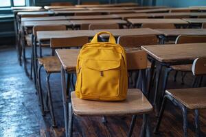 The yellow backpack sits prominently on a desk in a deserted classroom with vintage blue walls photo