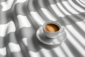 A warm cup of coffee resting on a white surface with soft shadows in the afternoon light photo