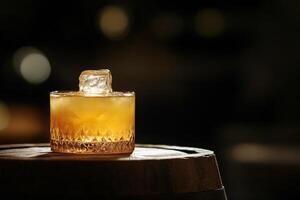 A glass of whiskey with ice resting on a wooden barrel in a warm, dimly lit environment photo