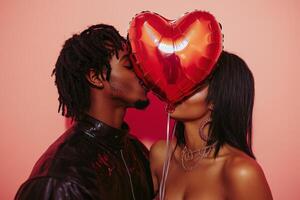 A couple shares a romantic kiss while hiding behind a red heart balloon against a pink background photo