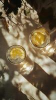 Refreshing glasses of lemonade with lemon slices and shadows from leaves on a bright surface photo