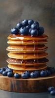 Stack of fluffy pancakes topped with blueberries and syrup on a wooden surface photo