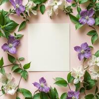 Purple flowers and green leaves surround blank textured paper on a neutral backdrop photo