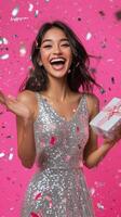 A joyful young woman celebrating with sparkling attire and confetti against a vibrant pink backdrop photo