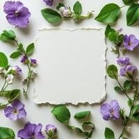 Purple flowers and green leaves surround blank textured paper on a neutral backdrop photo