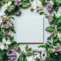 Purple flowers and green leaves surround blank textured paper on a neutral backdrop photo