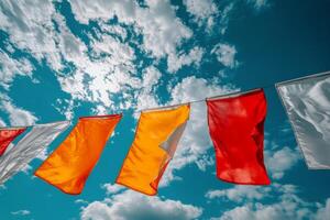 Colorful flags flutter against a bright blue sky featuring puffy clouds in the afternoon light photo