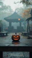 A carved pumpkin sits alone on a wooden surface in a foggy forest during autumn photo