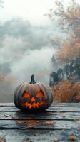 A carved pumpkin sits alone on a wooden surface in a foggy forest during autumn photo