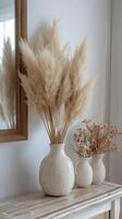 Pampas grass and dried flowers arranged in simple vases on a wooden table against a textured wall photo