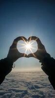 Two people forming a heart shape with their hands against a bright sun in a clear blue sky photo