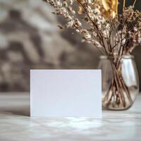 Simple blank card placed next to a vase of dried flowers in a modern interior setting photo
