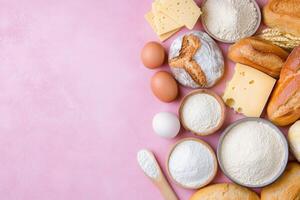Various baking ingredients including flour, eggs, cheese, and bread on a pink surface photo