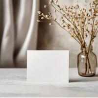Simple blank card placed next to a vase of dried flowers in a modern interior setting photo