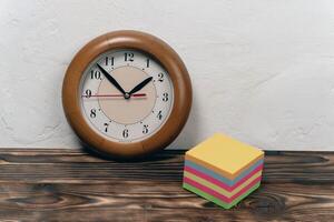 Wooden clock displays time next to colorful sticky notes on table photo