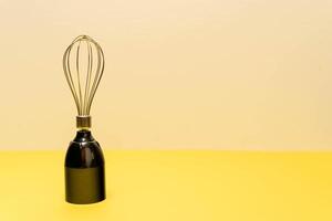 A modern whisk is positioned upright on a yellow surface photo
