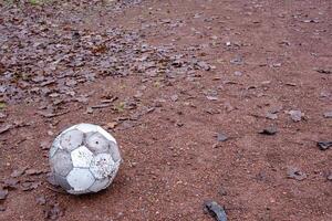 Old deflated soccer ball lying on a gravel field covered with dry leaves photo