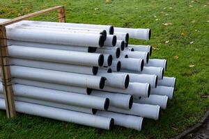 White plastic pipes stacked on green grass for construction photo