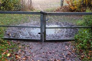 Closed metal gate preventing access to muddy puddle in autumn photo