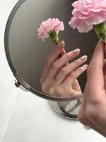 Reflection of a hand holding a pink flower in a circular mirror photo
