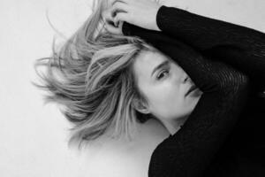 A woman with flowing hair poses elegantly on a light surface in black and white photo