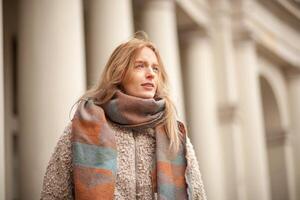 Woman in a cozy scarf walks near classical architecture on a sunny day photo