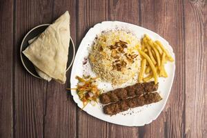 Beef Adana kebab with rice, french fries, salad and pita bread served in plate isolated on wooden table top view of turkish food photo