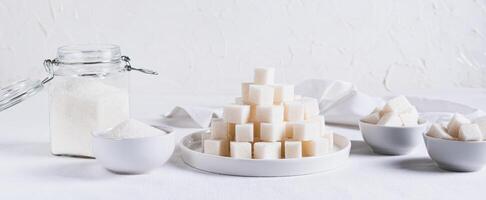 Lump sugar on a plate and granulated sugar in a bowl and jar on the table web banner photo