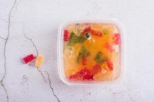 Closeup of gummy bears soaked in lemonade prepared for frozen candy in container on table top view photo