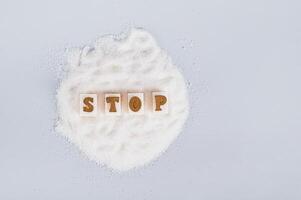 The word stop on pieces of refined sugar on granulated sugar on a blue background, top view photo