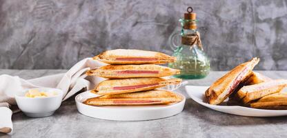 Grilled triangle sandwiches with cheese and sausage on a plate on a table web banner photo